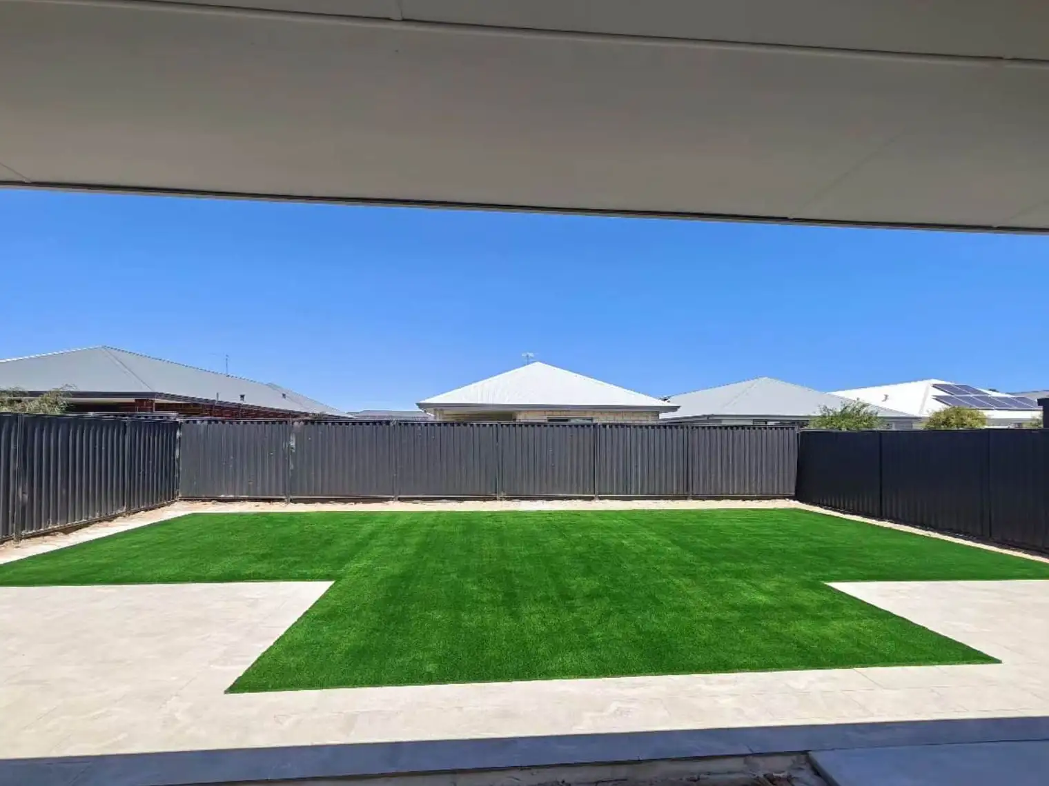 Backyard with a freshly installed artificial grass lawn and concrete paver border