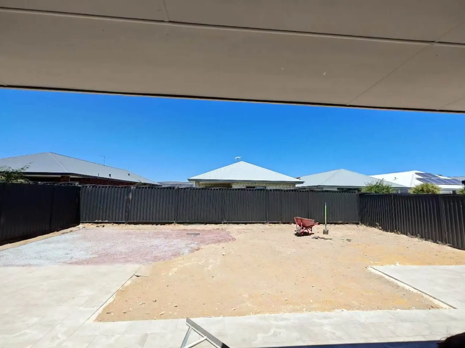Bare sandy backyard with red wheelbarrow and new Colorbond fencing, viewed from under the alfresco