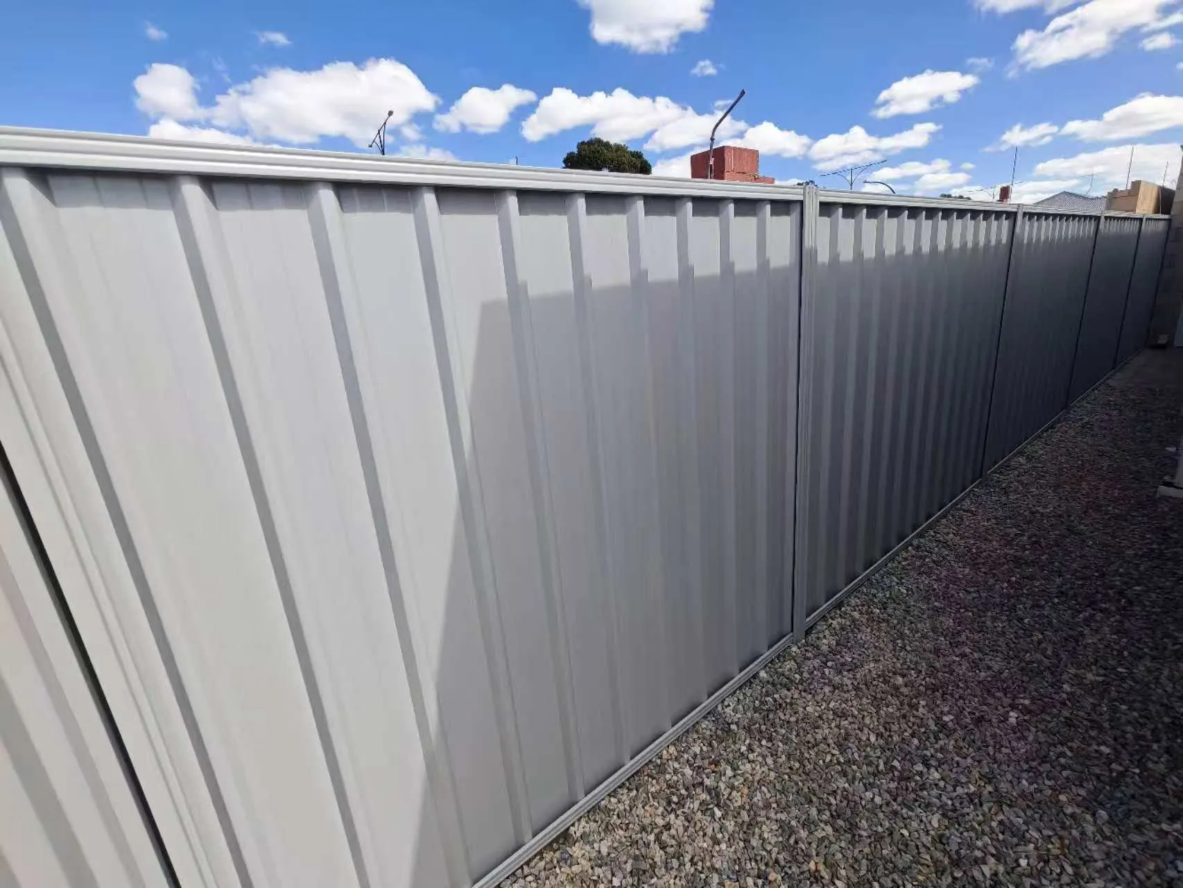 Newly installed grey Colorbond boundary fence under a blue sky