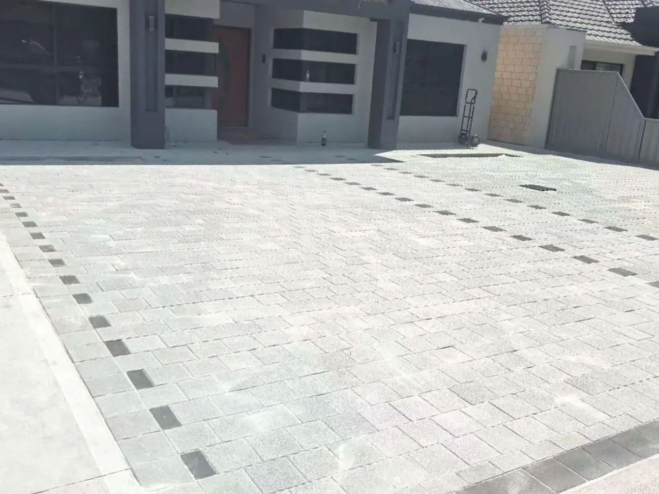 Large granite-look paver driveway with a charcoal accent band in front of a modern rendered house