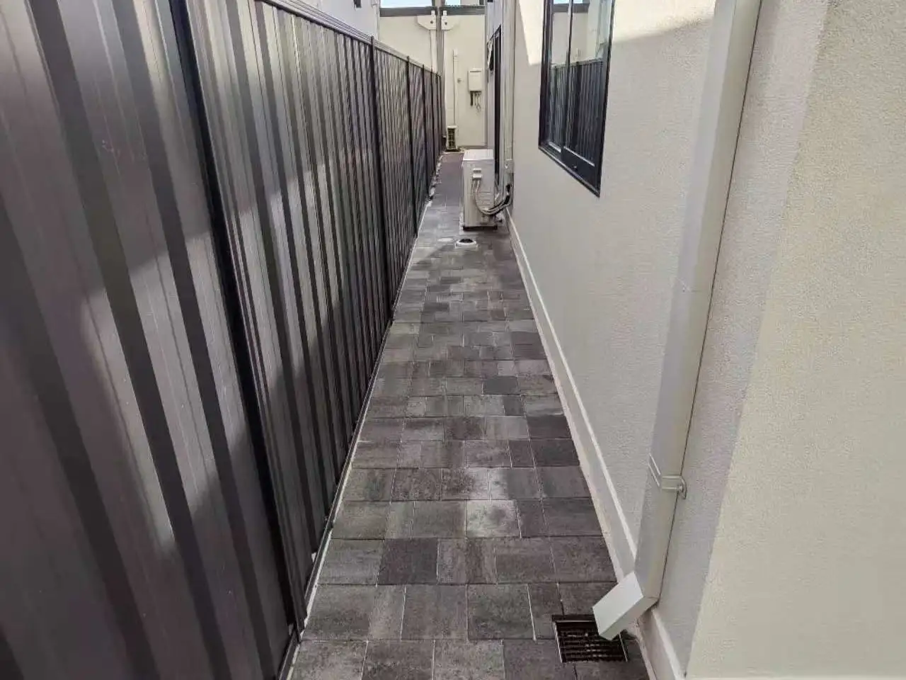 Finished side passage paved with charcoal stone pavers between a rendered wall and a Colorbond fence